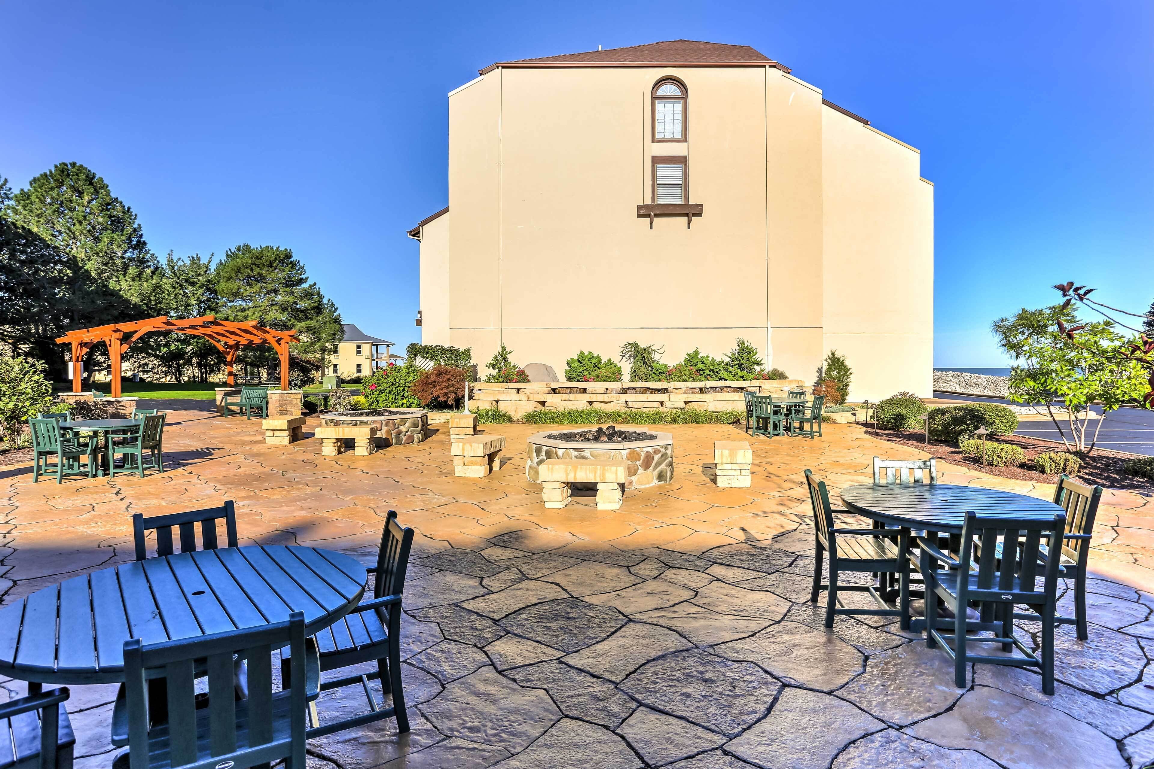A building with a beige exterior, a stone patio with outdoor seating, and a fire pit.
