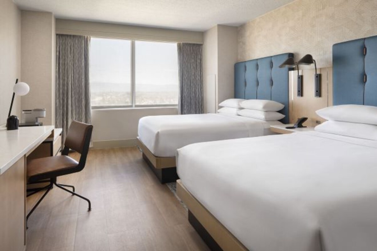Een hotelkamer met twee bedden, een bureau, een stoel en een raam met gordijnen.