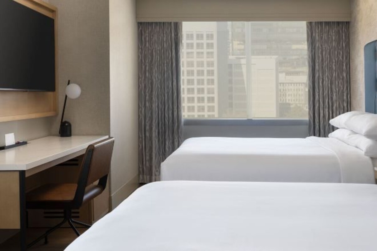 Een hotelkamer met twee bedden, een bureau, een stoel, een televisie en een raam met gordijnen.