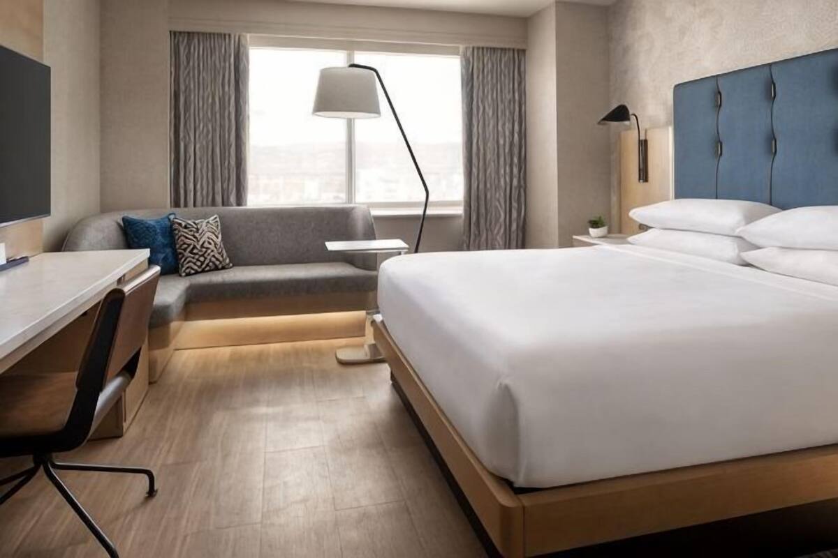 Une chambre d’hôtel avec un lit, un bureau, une chaise, un canapé, une lampe et une vue sur la ville.
