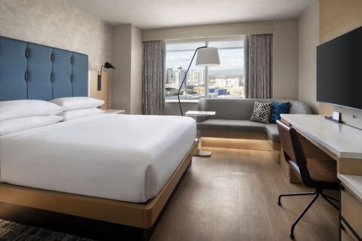 Een moderne hotelkamer met een groot bed, een bureau, een bank en uitzicht over de stad.