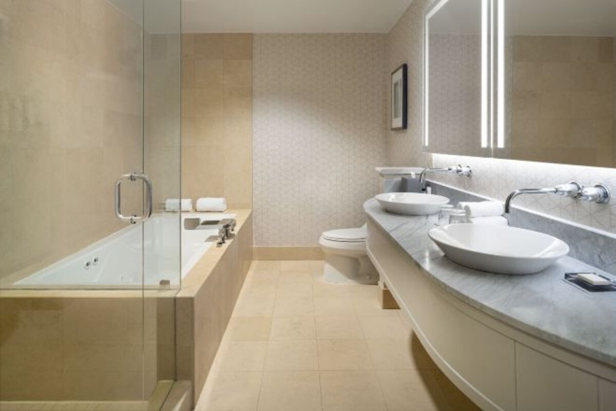 Een moderne badkamer met een douche in een glazen cabine, een wastafel met twee kommen en een toilet.