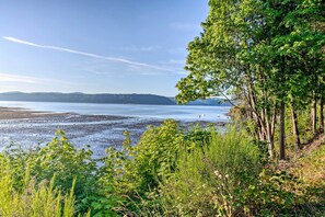 Un paysage côtier avec une plage, une végétation luxuriante et des collines à l’horizon.