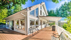 A large house with a wooden deck, multiple windows, and outdoor furniture. - Hood Canal Home w/ Hot Tub - Bordering Olympic NP! (Brinnon)