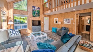 A spacious living area with a wooden interior, a sofa, a coffee table, and a staircase leading to an upper level. - Hood Canal Home w/ Hot Tub - Bordering Olympic NP! (Brinnon)