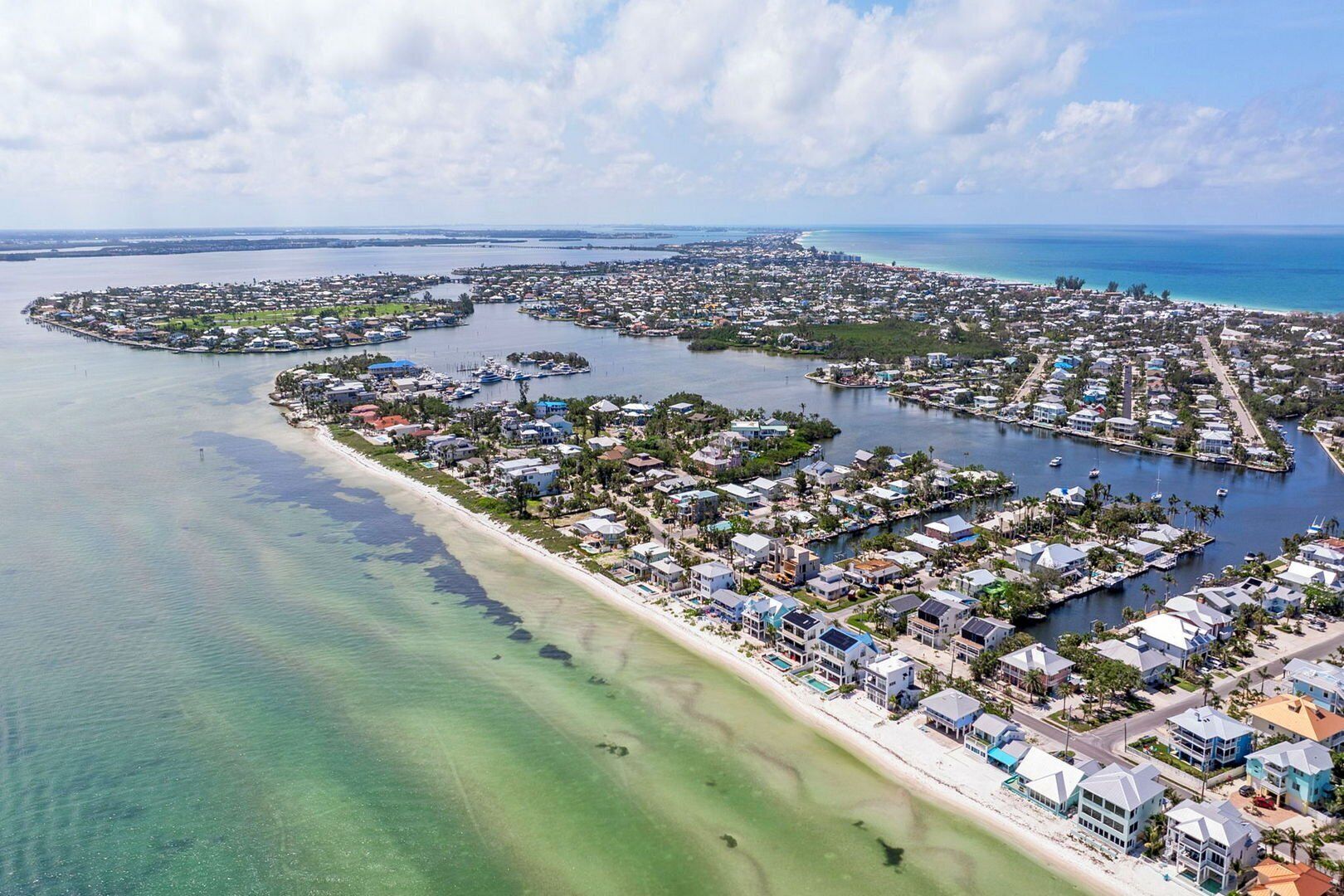 An aerial view of a coastal residential area with houses, a marina, and clear blue waters.