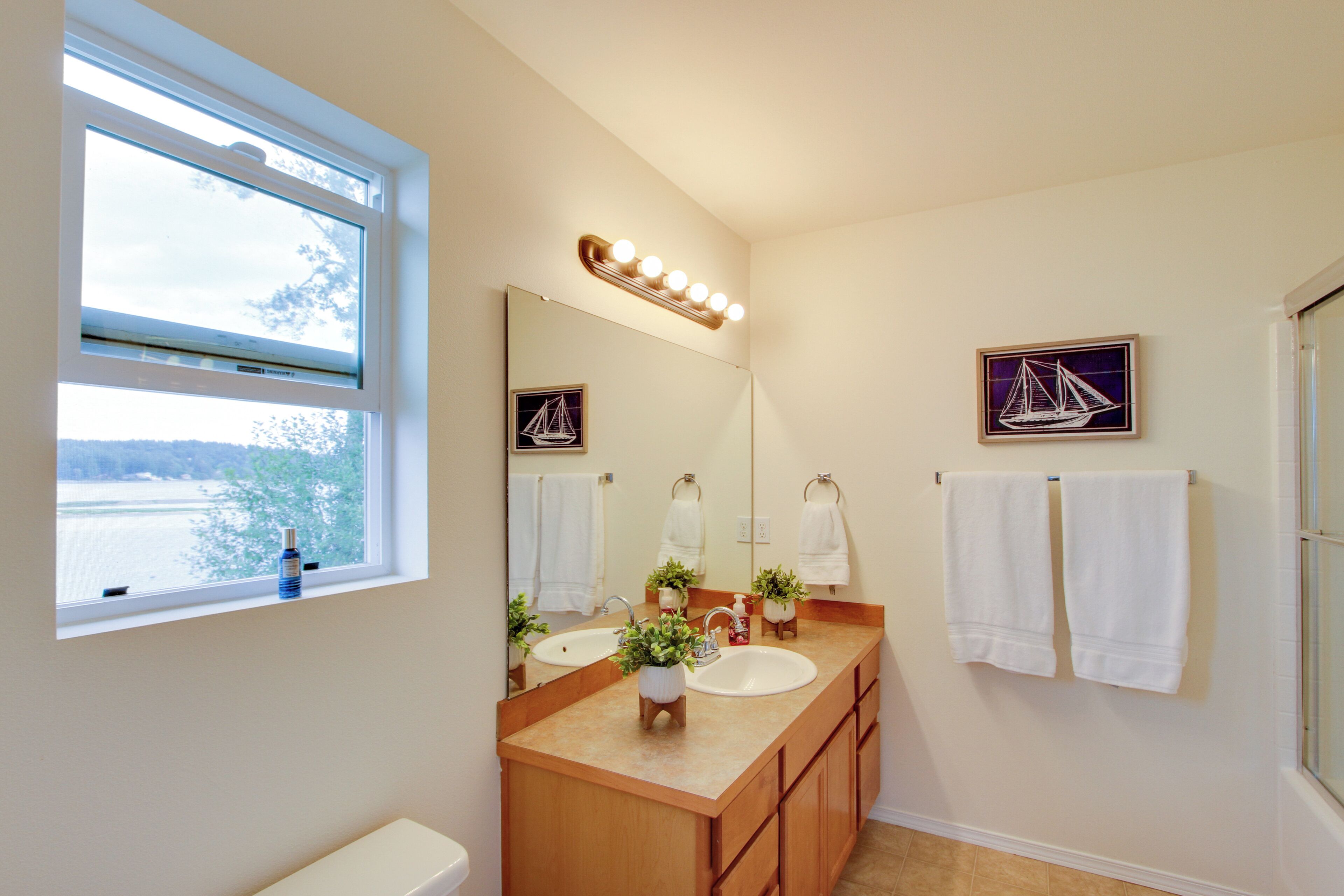 A bathroom with a large mirror, two sinks, a window, and a view of a body of water.