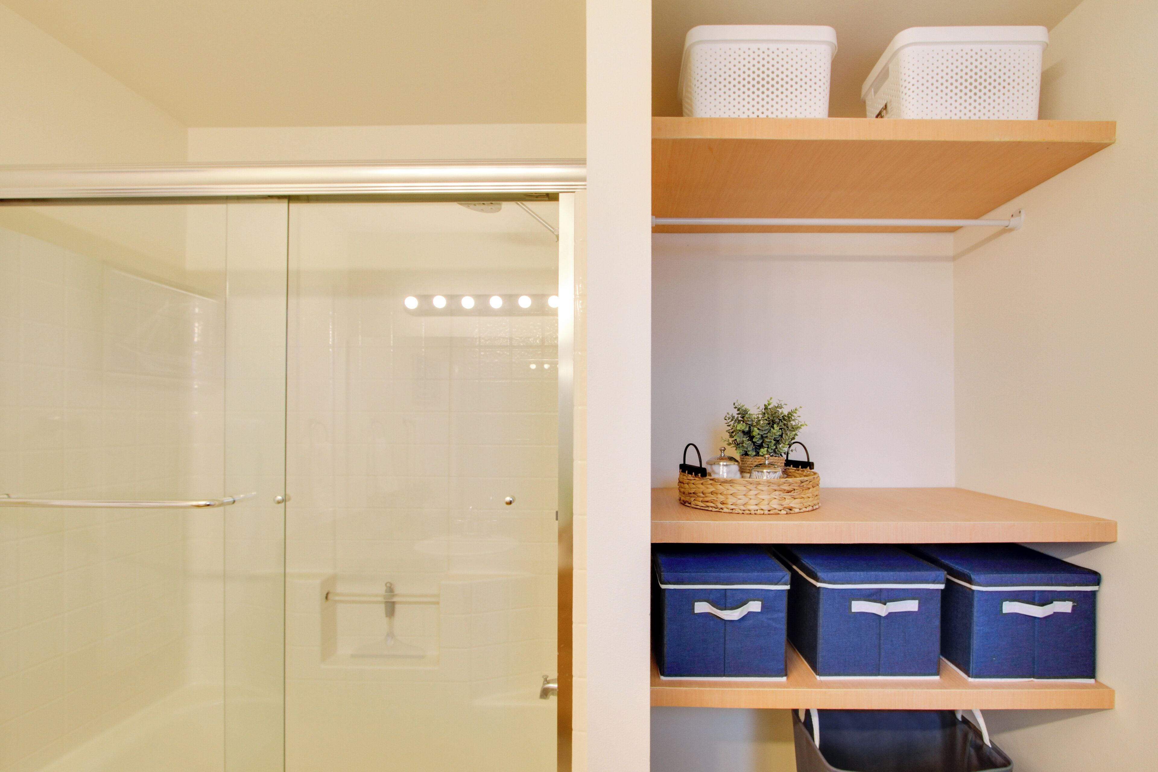 A bathroom with a glass shower door, a towel rack, and a shelf with storage boxes and a basket.