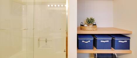 A bathroom with a glass shower door, a towel rack, and a shelf with storage boxes and a basket.