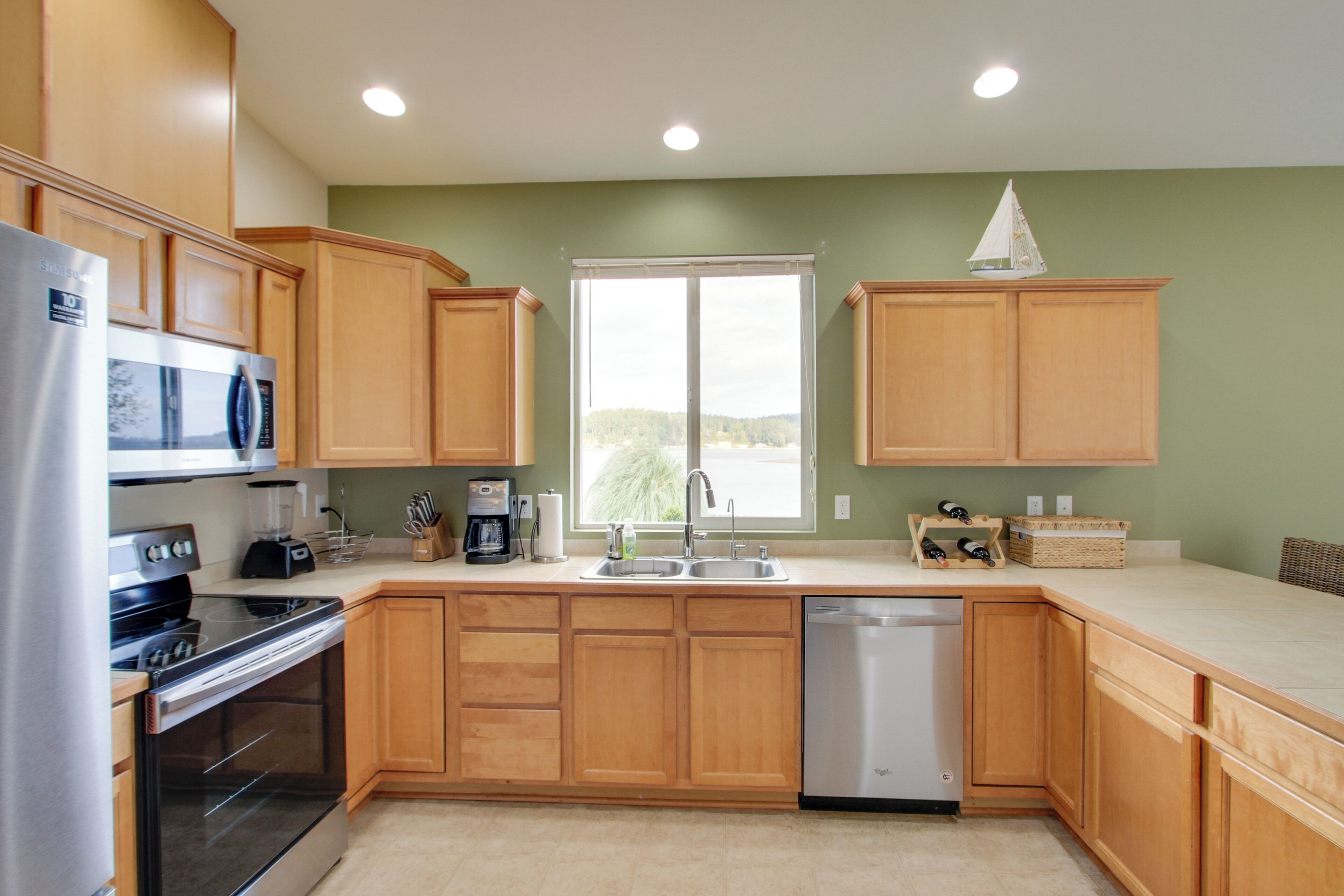 A kitchen with wooden cabinets, a stainless steel refrigerator, a dishwasher, and a window with a view of trees.