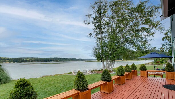 A wooden deck with benches and planters, overlooking a lake with a clear sky. - Waterfront Allyn Home With Fire Pit + 2 Kayaks! (Allyn)