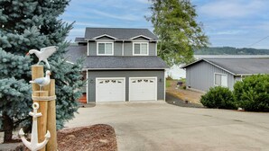 A two-story house with a garage, a dock, and a bird sculpture. - Waterfront Allyn Home With Fire Pit + 2 Kayaks! (Allyn)