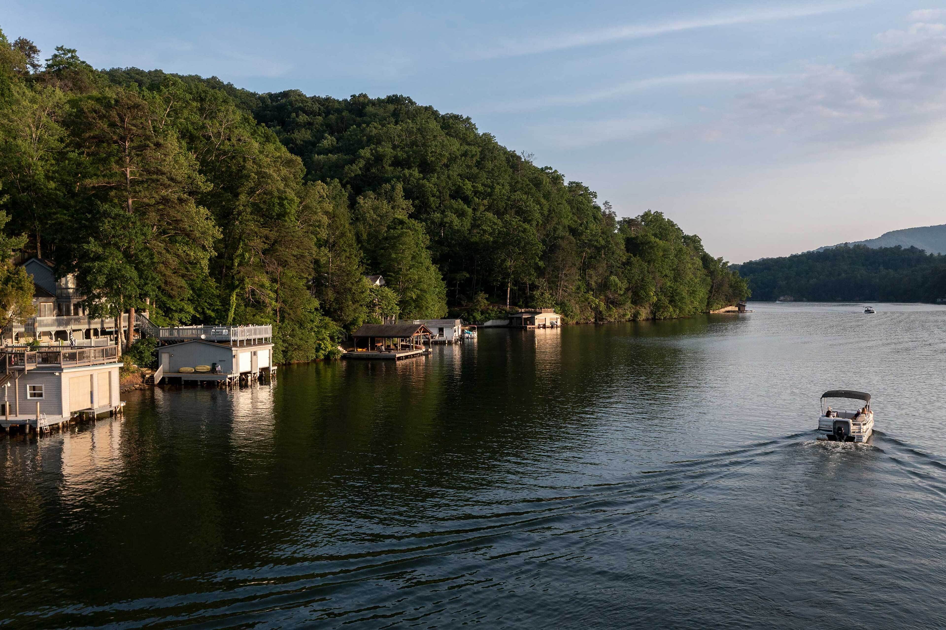 A lakeside property with floating homes, a boat on the water, and dense forested hills in the background.
