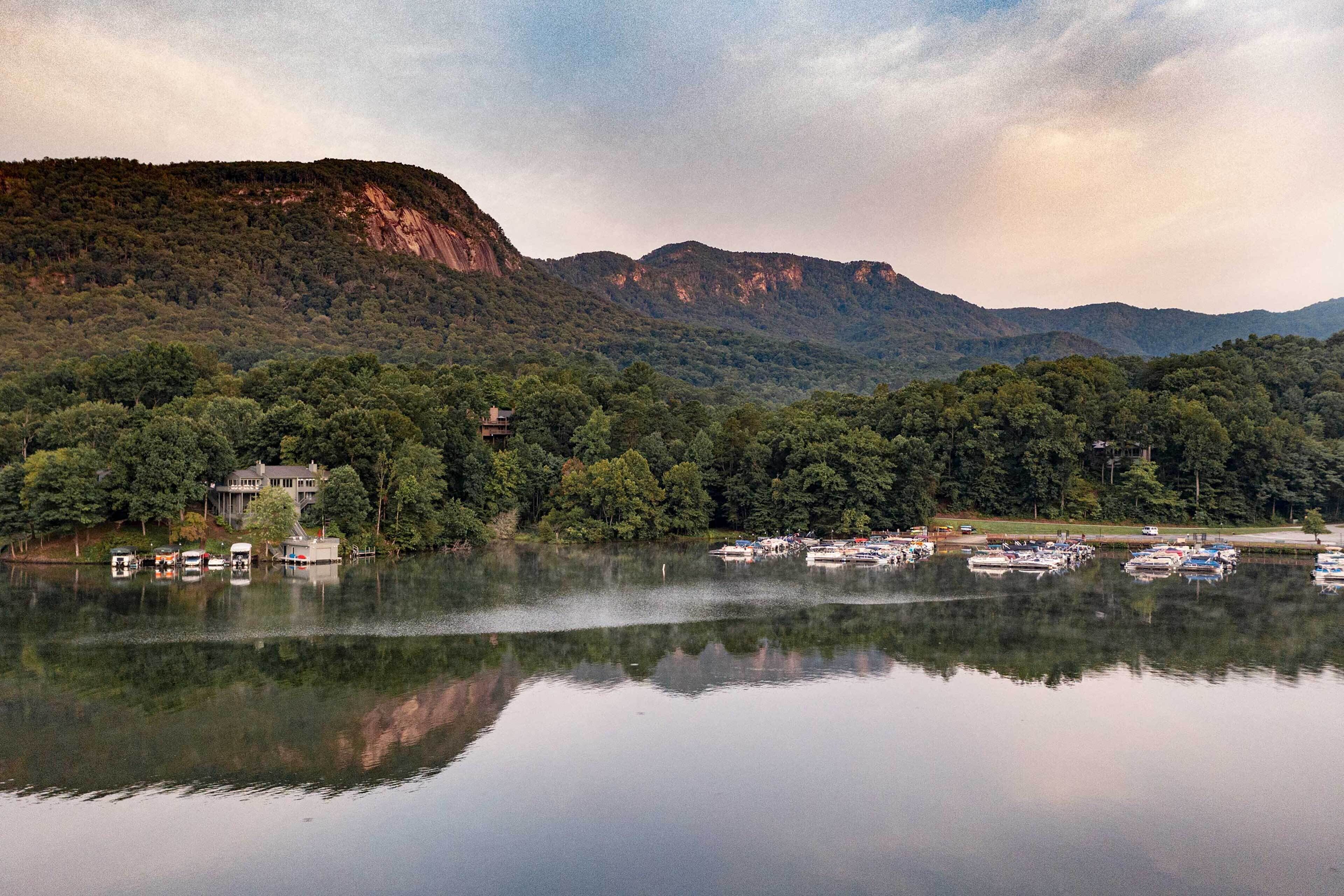 Un lac avec des bateaux, une maison et, au loin, des collines boisées.