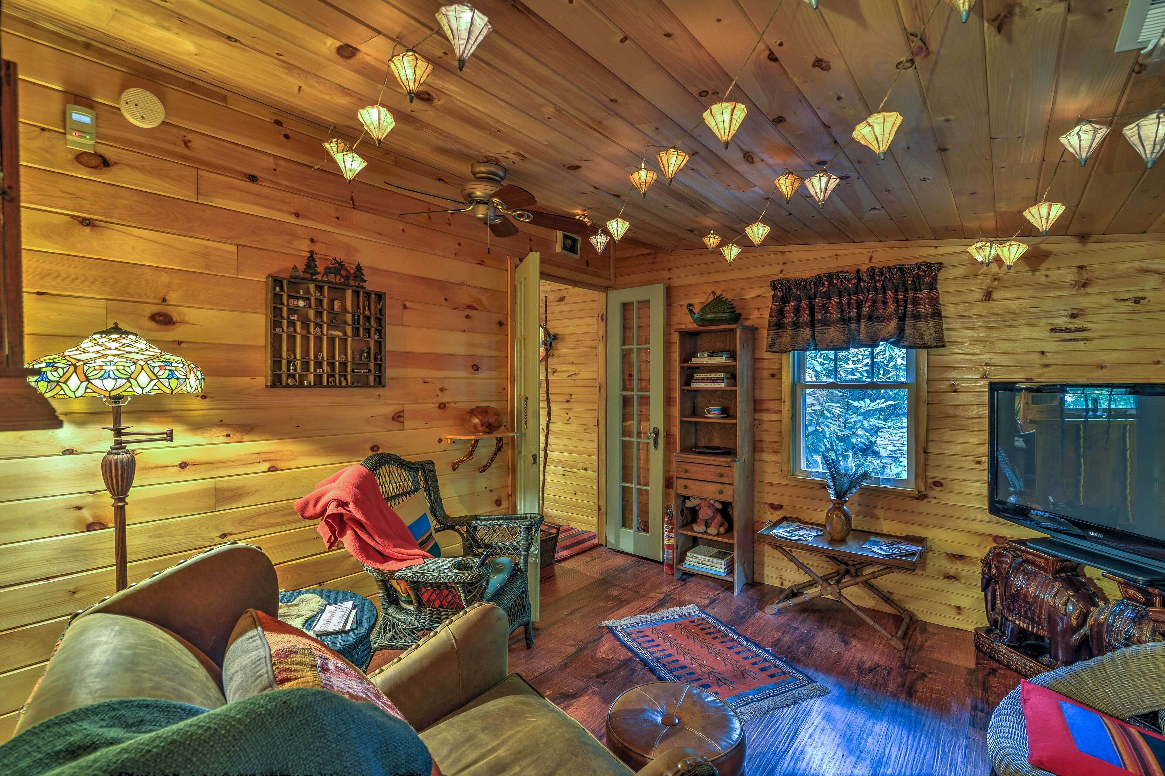 Un intérieur de chalet chaleureux avec des murs en bois, un ventilateur de plafond, un téléviseur et différents types de sièges.