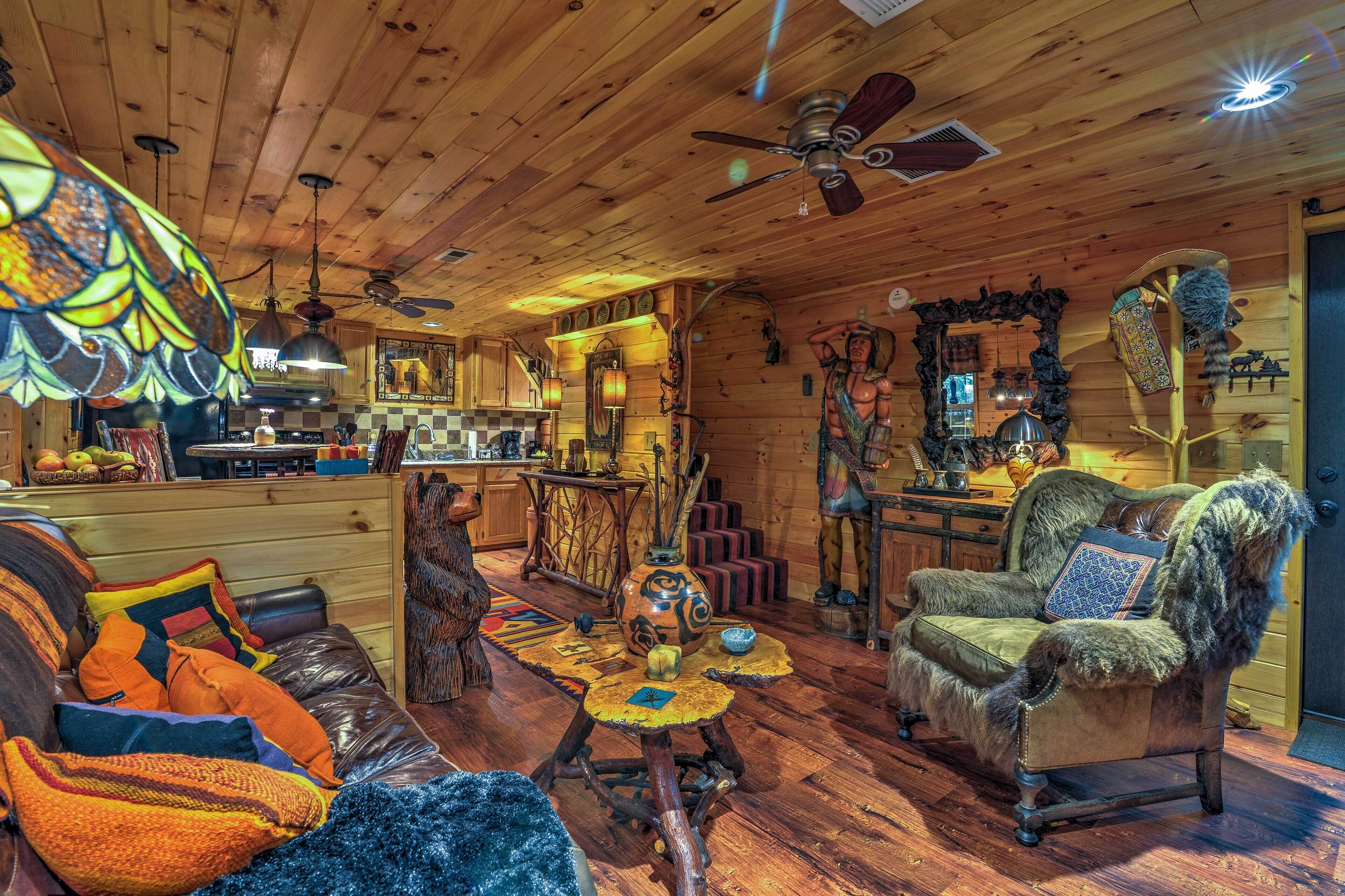 Ein gemütliches Blockhaus-Interieur mit Holzbalkendecke, einem Essbereich, einem Wohnzimmer mit Sofa und Sesseln sowie einem Kamin.