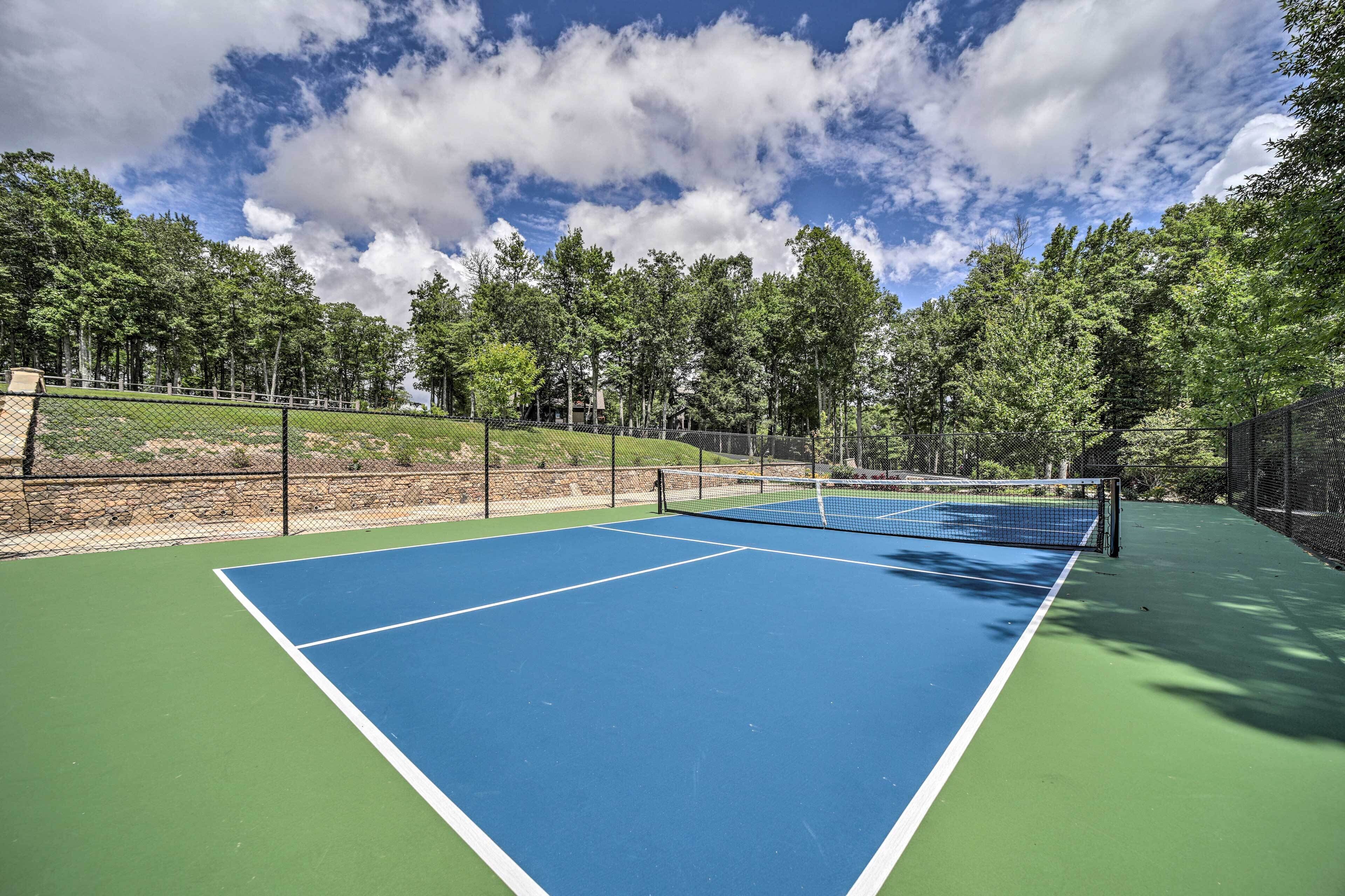 A tennis court with a net, surrounded by a fence and trees.