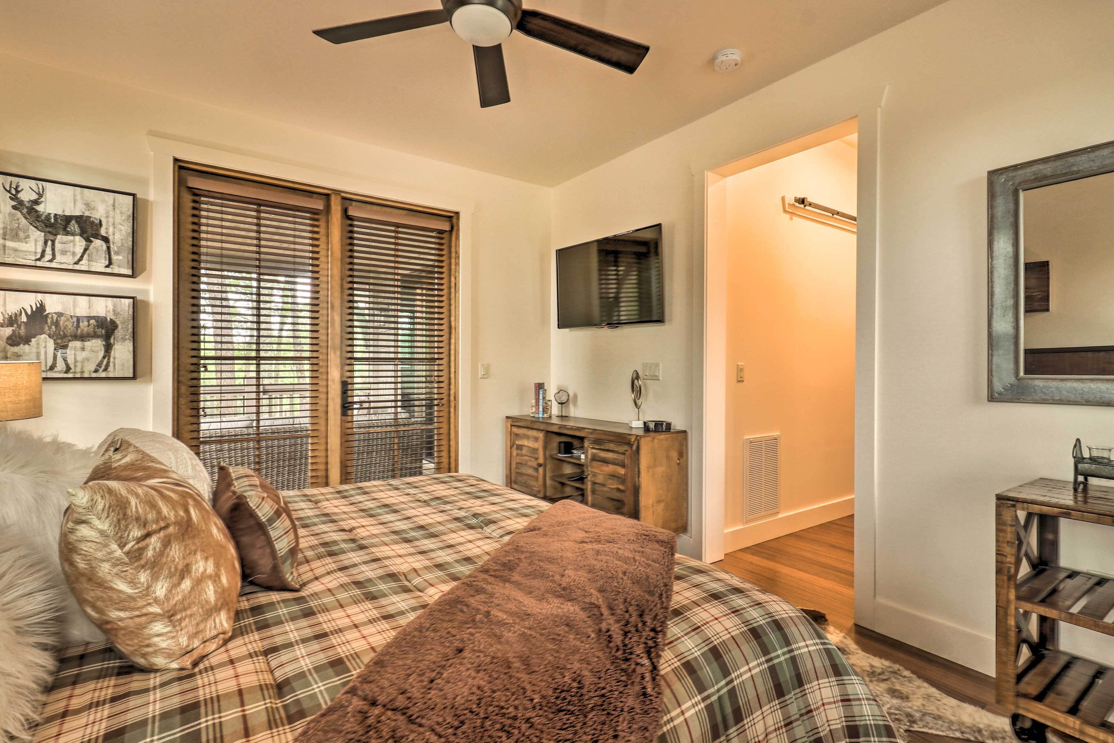 A bedroom with a bed, a ceiling fan, a dresser, a mirror, and a television.