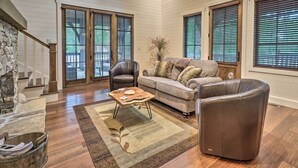 A spacious living room with a stone fireplace, a leather sofa, a coffee table, and large windows with blinds. - Hike, Fish & Golf! Serene Mtn Retreat in Glenville (Glenville)