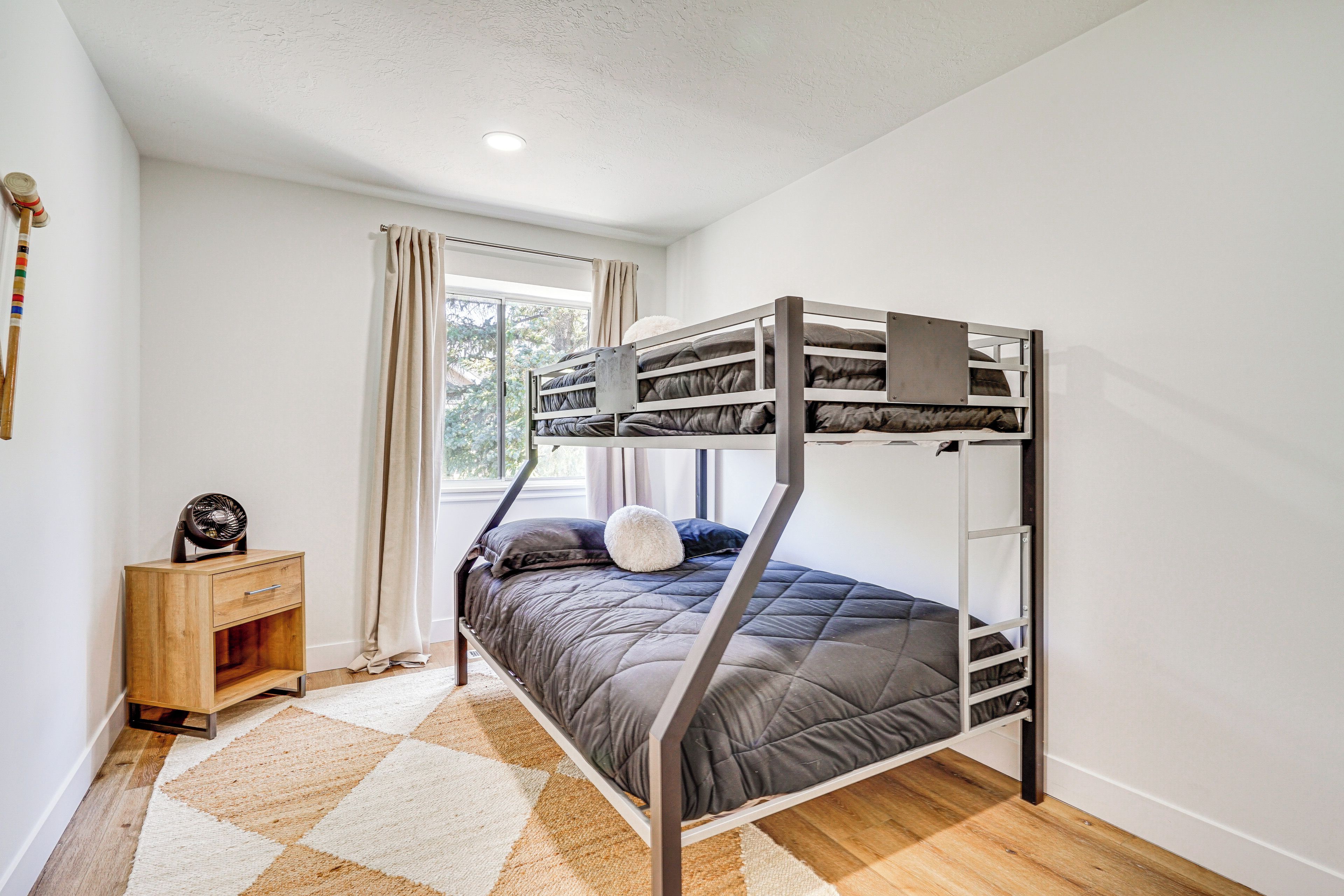 A bunk bed in a room with a window, a small wooden nightstand, and a checkered rug.
