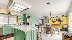 A kitchen with green cabinets, a central island, and a dining area with wooden chairs and a table. - Pleasant Valley Wine Trail Home - Near Paso Robles (San Miguel)
