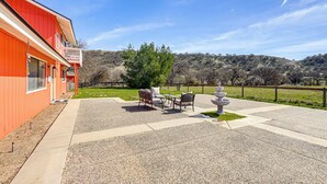 A red building with a balcony, a patio with outdoor furniture, and a view of a hilly landscape. - Pleasant Valley Wine Trail Home - Near Paso Robles (San Miguel)