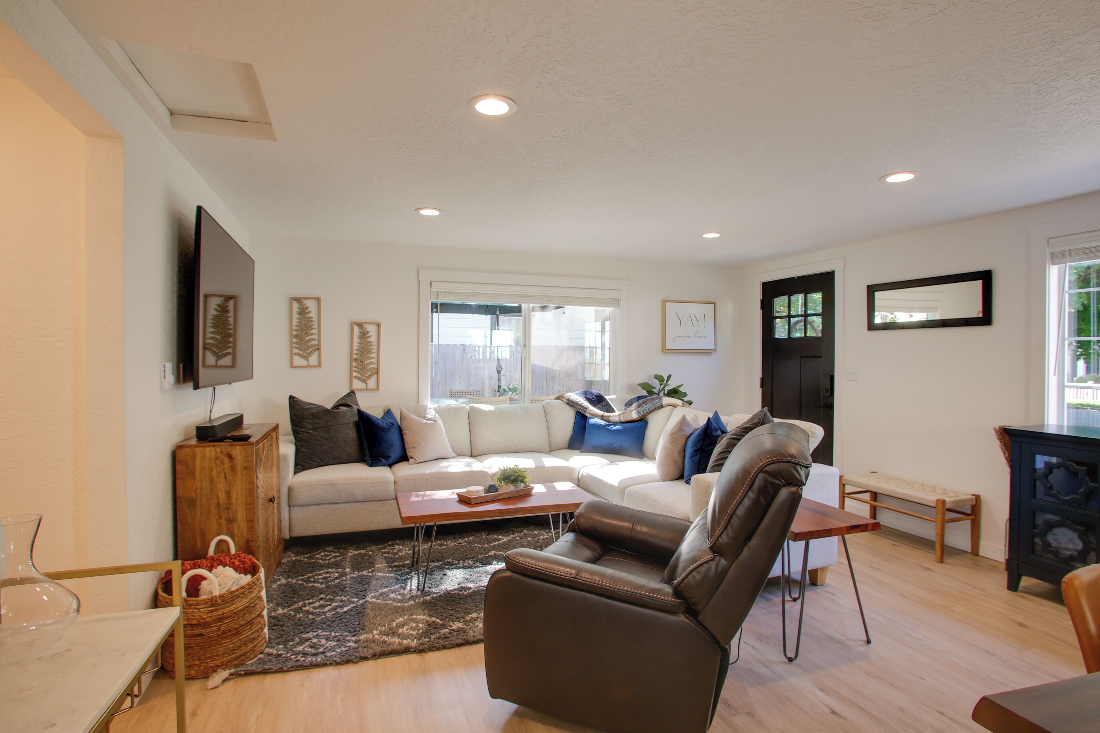 A living room with a sofa, coffee table, and a brown leather chair. There is a wooden cabinet, a wicker basket, and a small table with a vase.