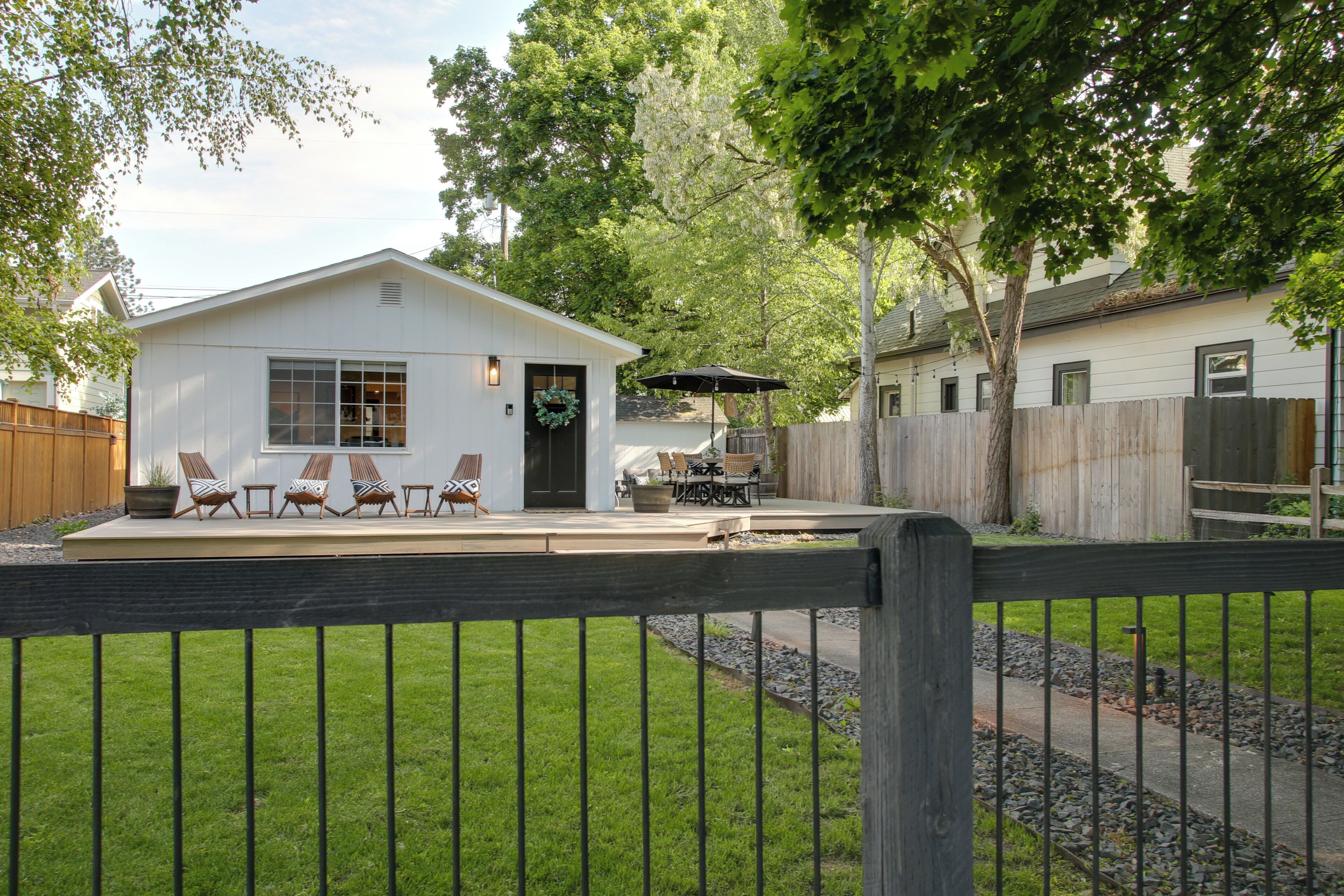 A white single-story house with a covered patio area, a fenced backyard, and a wooden deck.