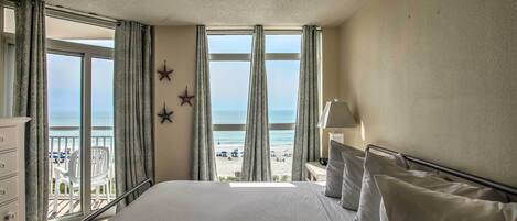 Ein Hotelzimmer mit einem großen Bett, Meerblick und einem Balkon mit Sitzgelegenheiten.