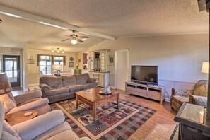 A living room with a sofa, coffee table, TV, and a kitchen area in the background. - White River Fishing Escape w/ Deck & Patio! (Cotter)