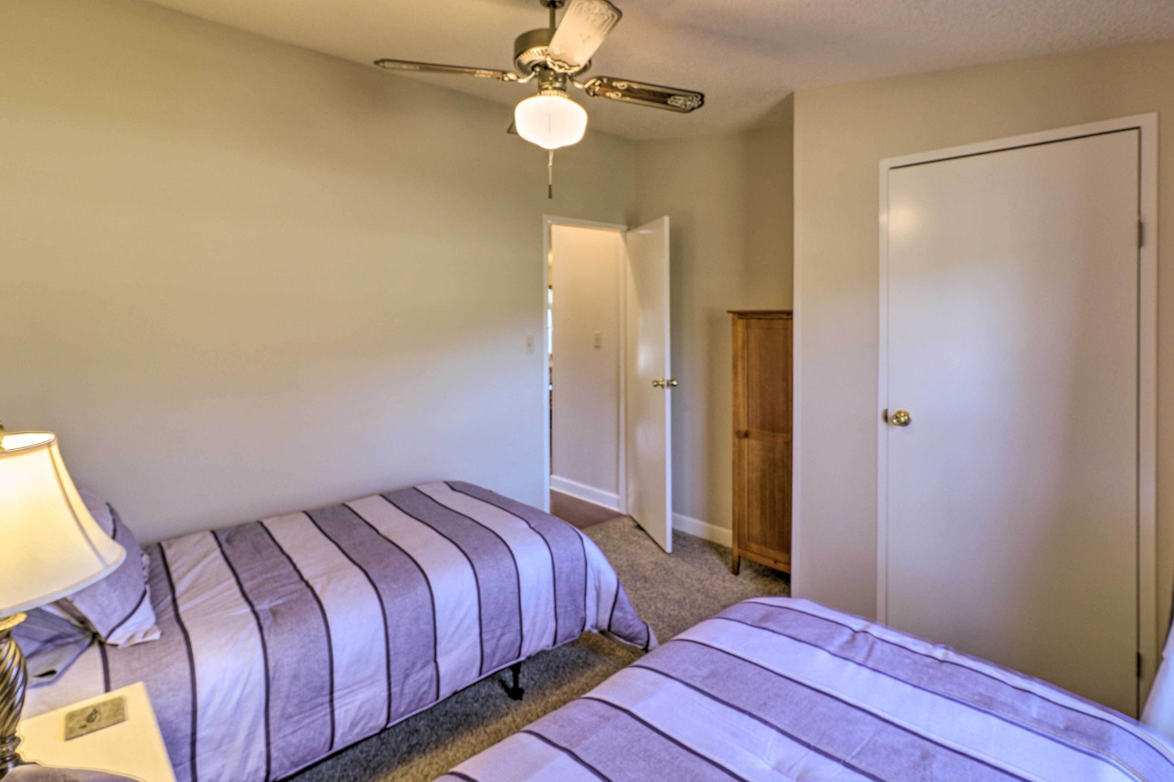 Une chambre avec deux lits, un ventilateur de plafond, une porte et une lampe.
