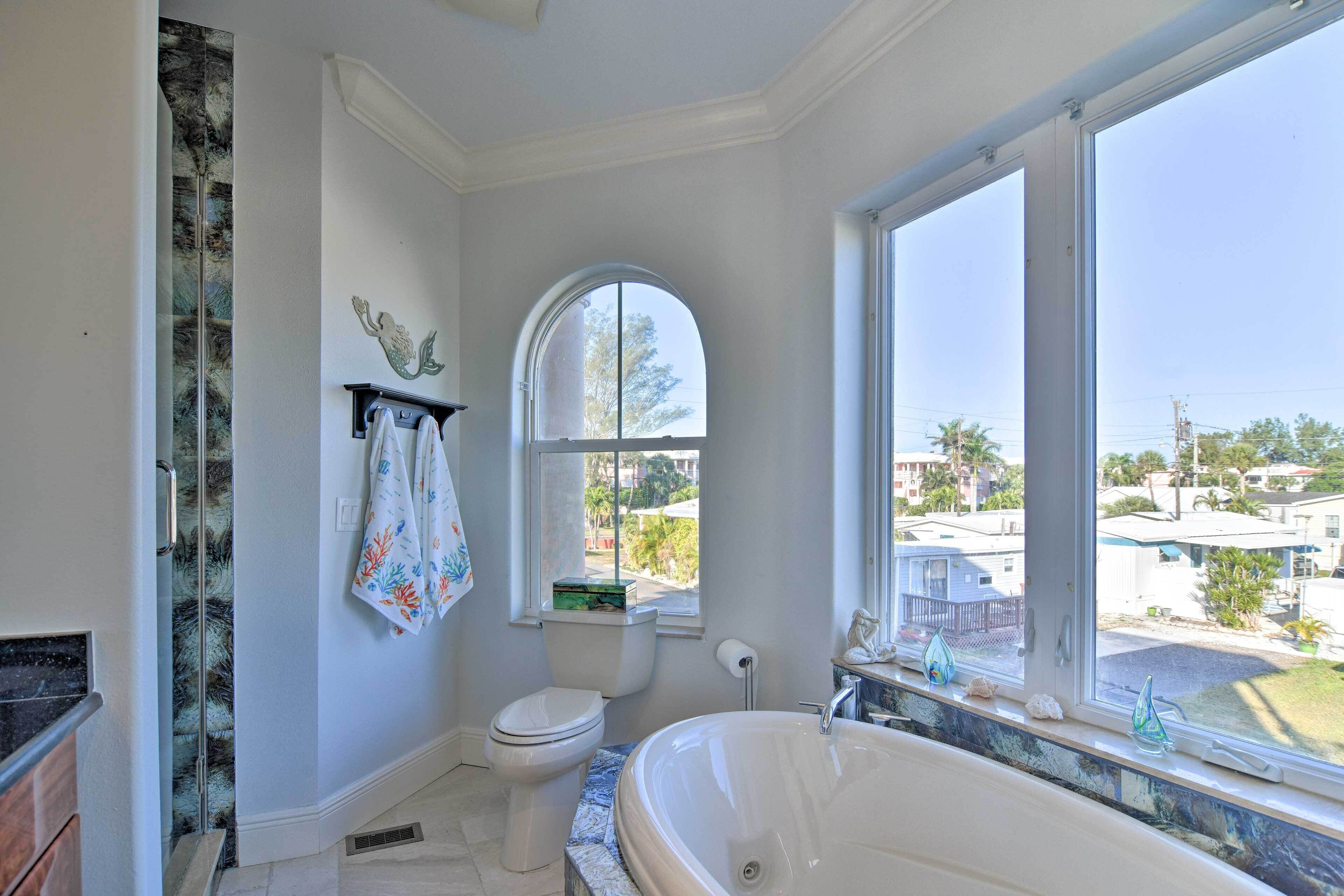 A bathroom with a large bathtub, a toilet, and a window with a view of the neighborhood.