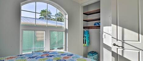Un dormitorio con un ventanal grande, una cama con colcha colorida y un armario con estantes.
