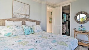 A bedroom with a bed, a wall-mounted sailboat painting, a round mirror, and a wicker side table with glassware. - Bradenton Townhome - Walk to Locals-only Beach! (Bradenton Beach)