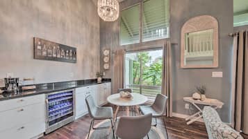 A modern kitchen with a wine cooler, a dining table with chairs, and a large window with curtains.