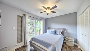 A bedroom with a bed, a ceiling fan, a window with curtains, and a small round ottoman. - Coastal Escape Condo w/ Pool, Near Beaches! (Princeville)