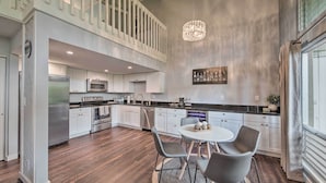 A modern kitchen with a dining area, featuring a chandelier, stainless steel appliances, and a view of the outdoors. - Coastal Escape Condo w/ Pool, Near Beaches! (Princeville)