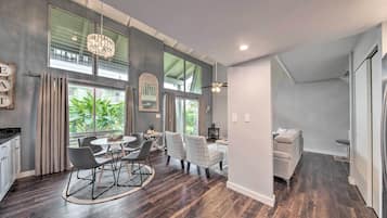 A modern kitchen with dark wood flooring, a dining area with a round table and chairs, and a living area with a sofa and a TV.