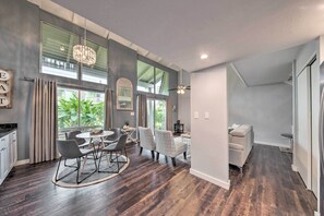 A modern kitchen with dark wood flooring, a dining area with a round table and chairs, and a living area with a sofa and a TV.