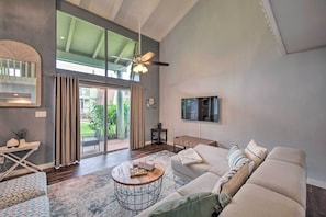 Un ampio soggiorno con una grande finestra, una ventola a soffitto, un divano, un tavolino e una TV montata a parete.