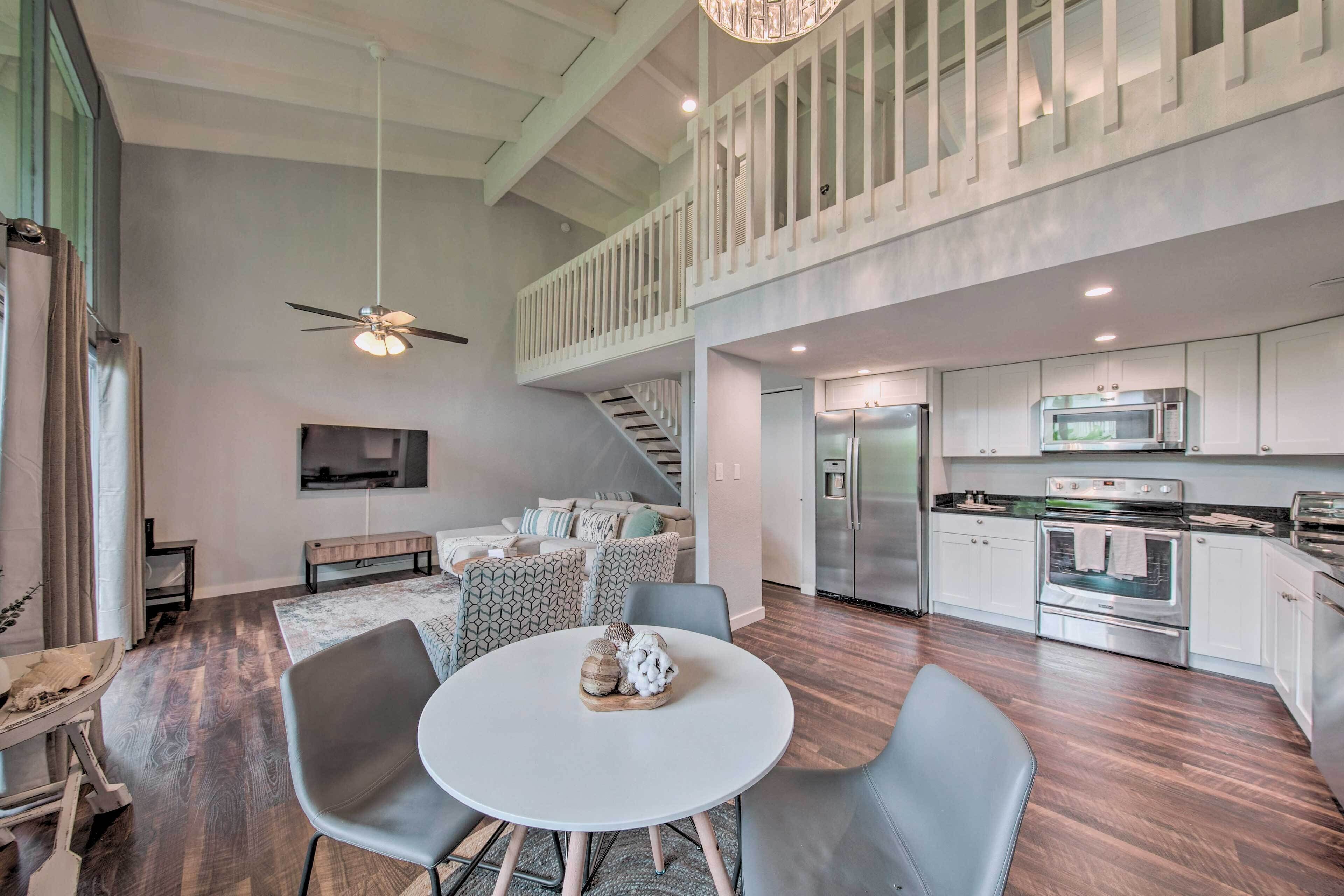 A modern kitchen with stainless steel appliances, a dining area with a round table and chairs, and a staircase leading to an upper level.