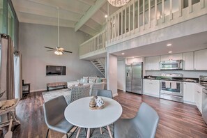 A modern kitchen with stainless steel appliances, a dining area with a round table and chairs, and a staircase leading to an upper level.