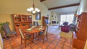 Uma sala de jantar com mesa e cadeiras de madeira, um candelabro e uma lareira ao fundo.