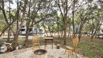 A campsite with a fire pit, wooden chairs, and a table.