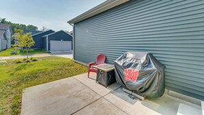 Une façade de maison avec un garage, un barbecue couvert, une chaise rouge et une petite table.