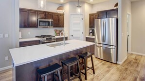 Une cuisine moderne avec des meubles en bois foncé, des appareils en acier inoxydable, un îlot central blanc avec des tabourets et un éclairage suspendu.