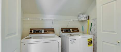 A laundry room with two stacked washers and dryers, a shelf with cleaning supplies, and a door with a doorknob.