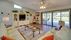 Un salón amplio con televisor grande, asientos cómodos, ventilador de techo y vistas al exterior.