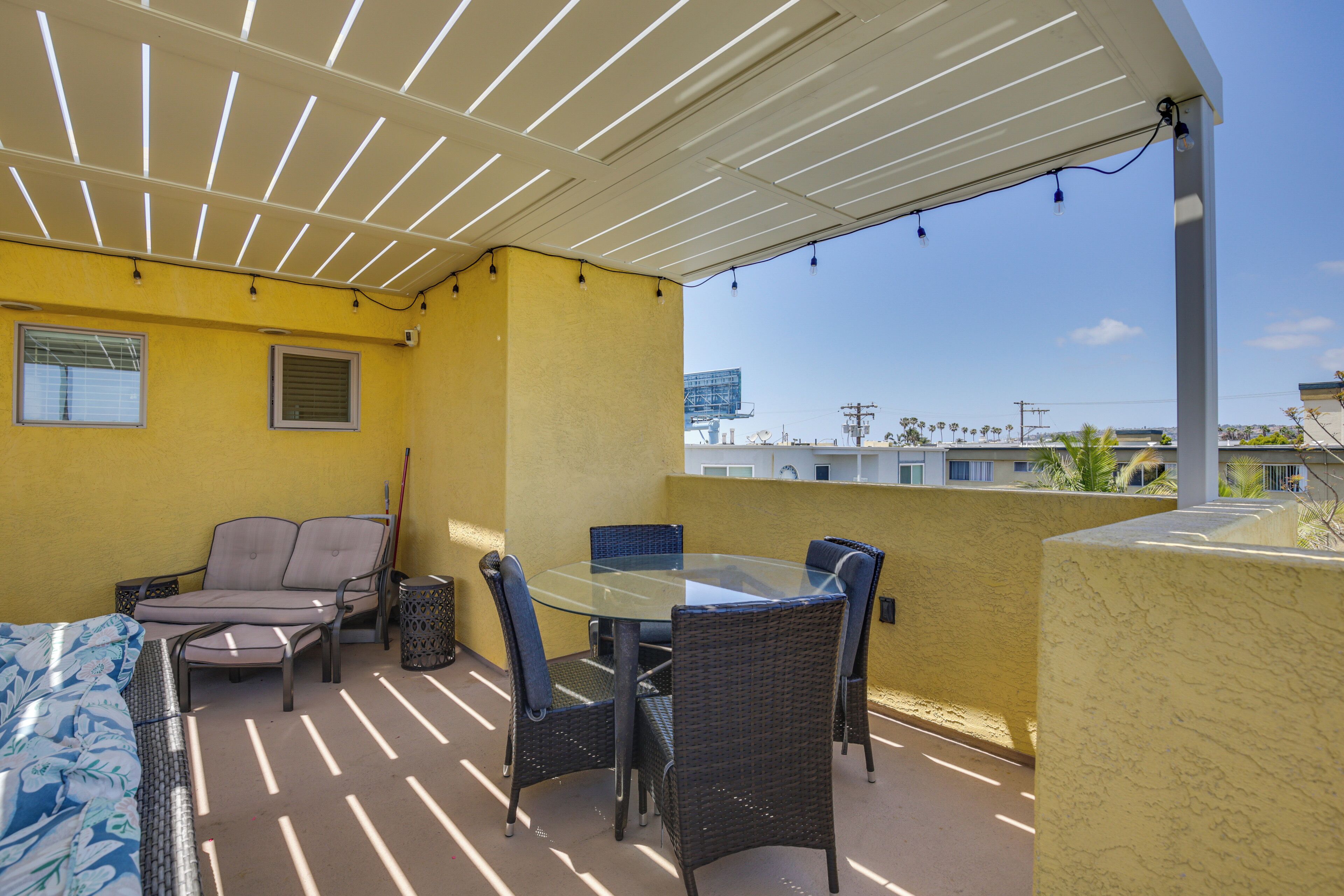 A covered patio with a glass table and wicker chairs, yellow walls, and a view of the cityscape.