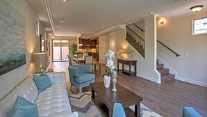 Un salon spacieux avec un canapé blanc, des fauteuils bleus, une table basse en bois et un escalier menant à l’étage supérieur.